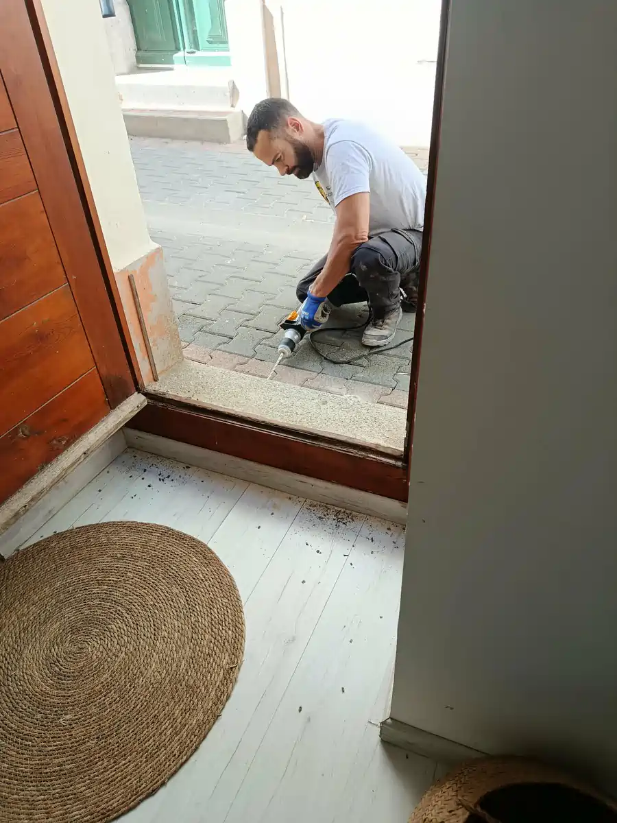 Intervenant perçant le seuil maçonné d'une porte d'entrée pour poser une barrière anti-termites